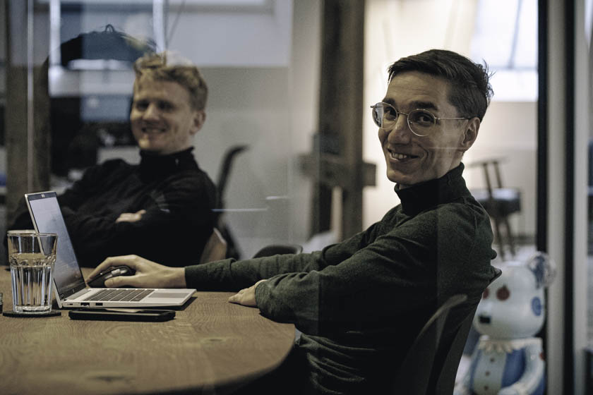 Zwei Mitarbeiter lachen bei Meetingsituation in die Kamera